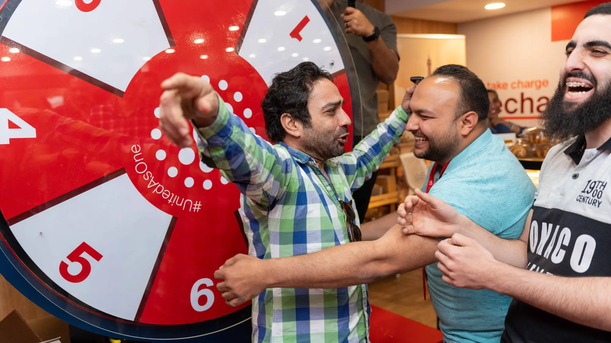 Colleagues cheering and laughing beside a prize spin wheel at an office anniversary party