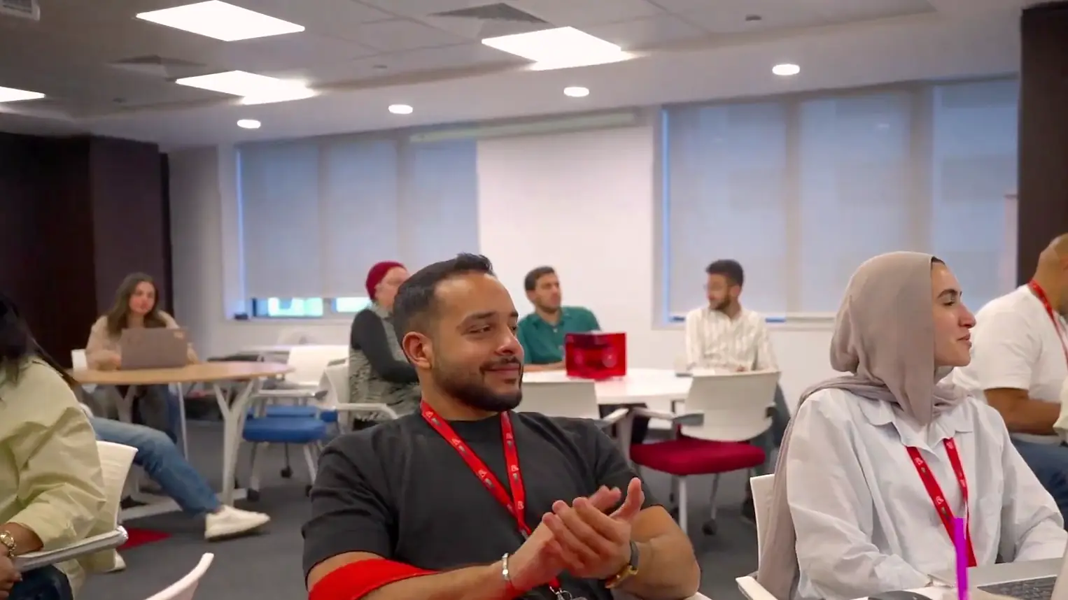 Smiling colleague applauding at round tables as coworkers look on during an anniversary gathering in a bright meeting room