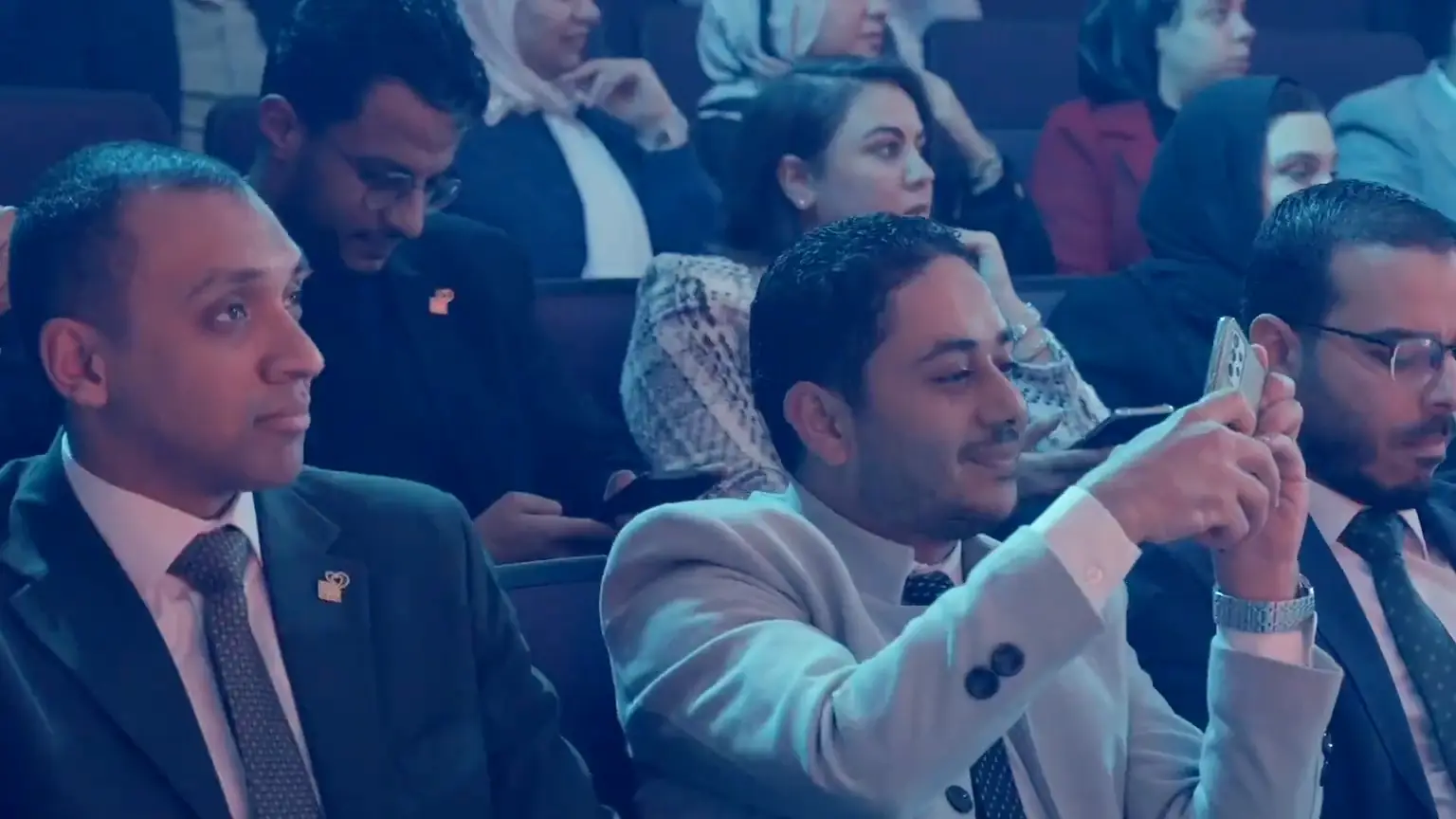 Guests in the audience smile and film the ceremony on their phones