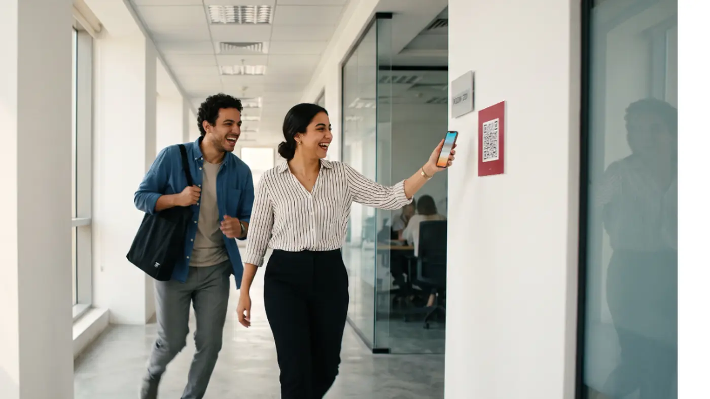 Two colleagues laugh as one scans a QR code on a corridor wall during a security game