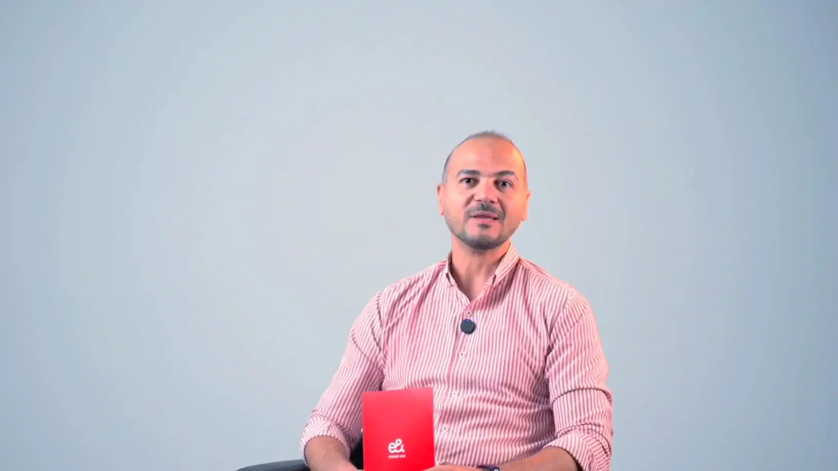 A father in a pink striped shirt speaks to camera, holding an e& card