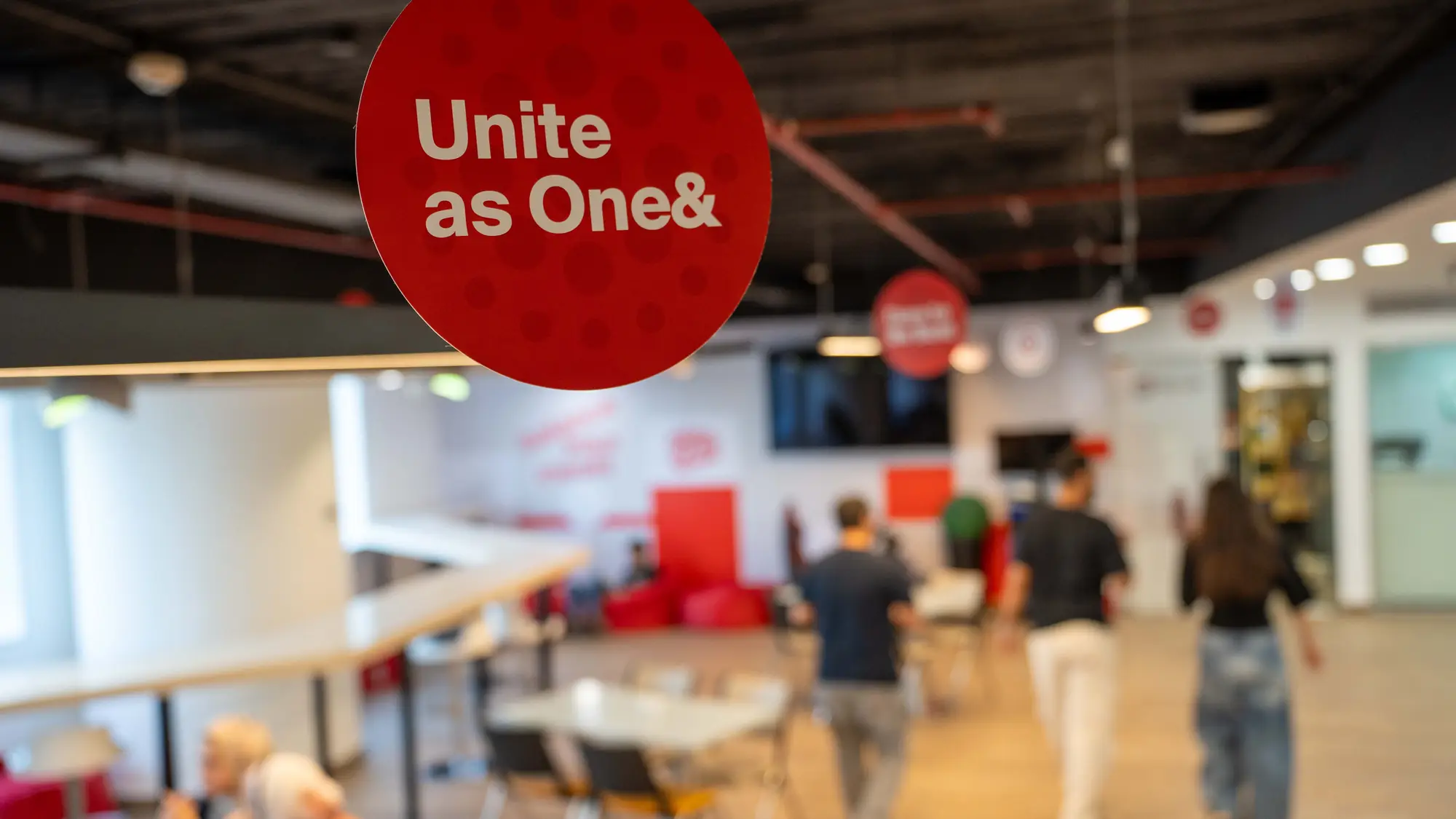 A round red values dangler hangs above an open-plan office as staff walk past
