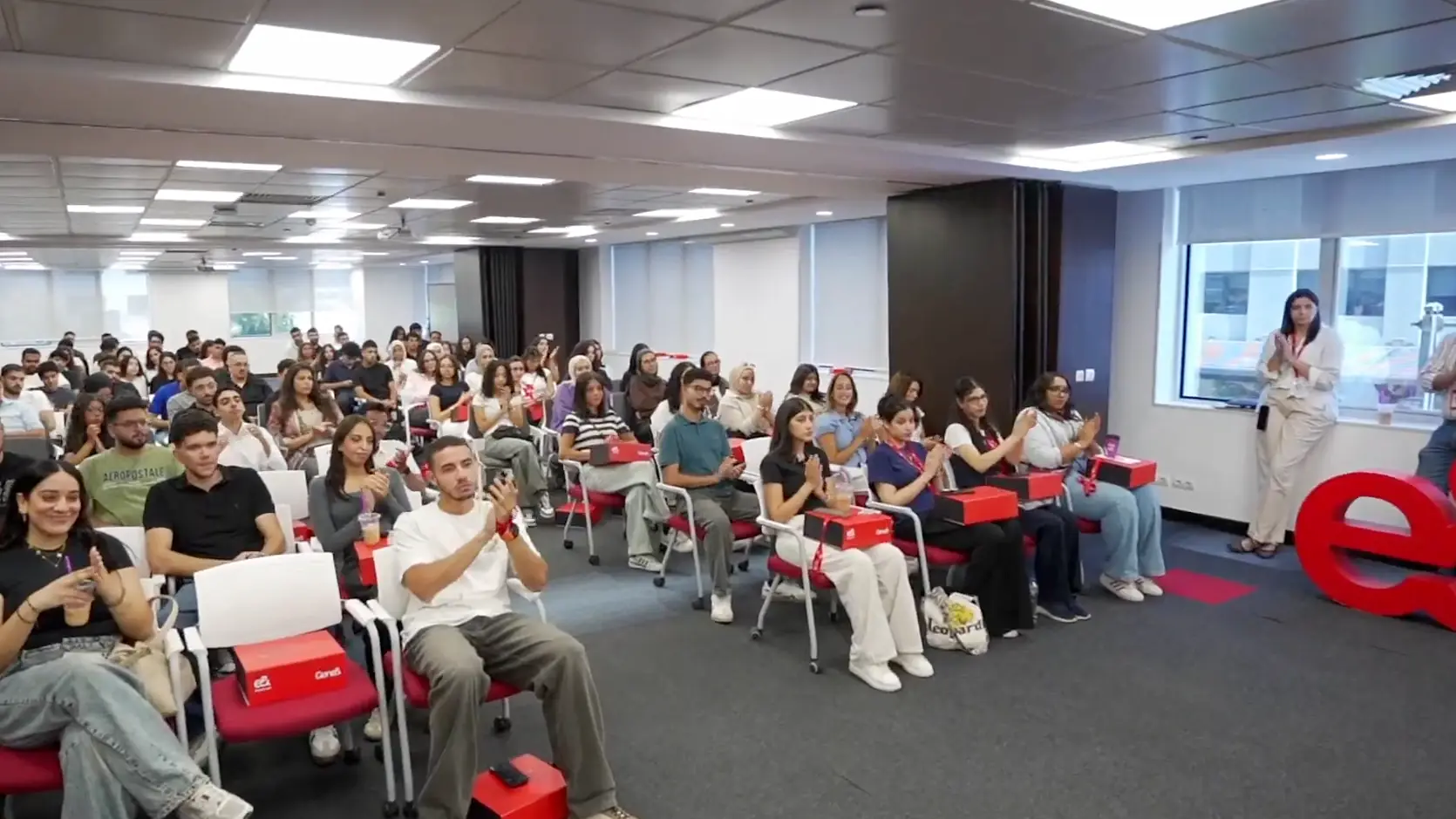 Packed training room of interns clapping in rows, welcome kits on their laps