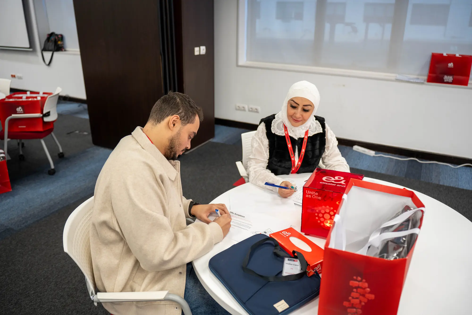 Two new employees filling in first-day paperwork beside their branded welcome box and bag