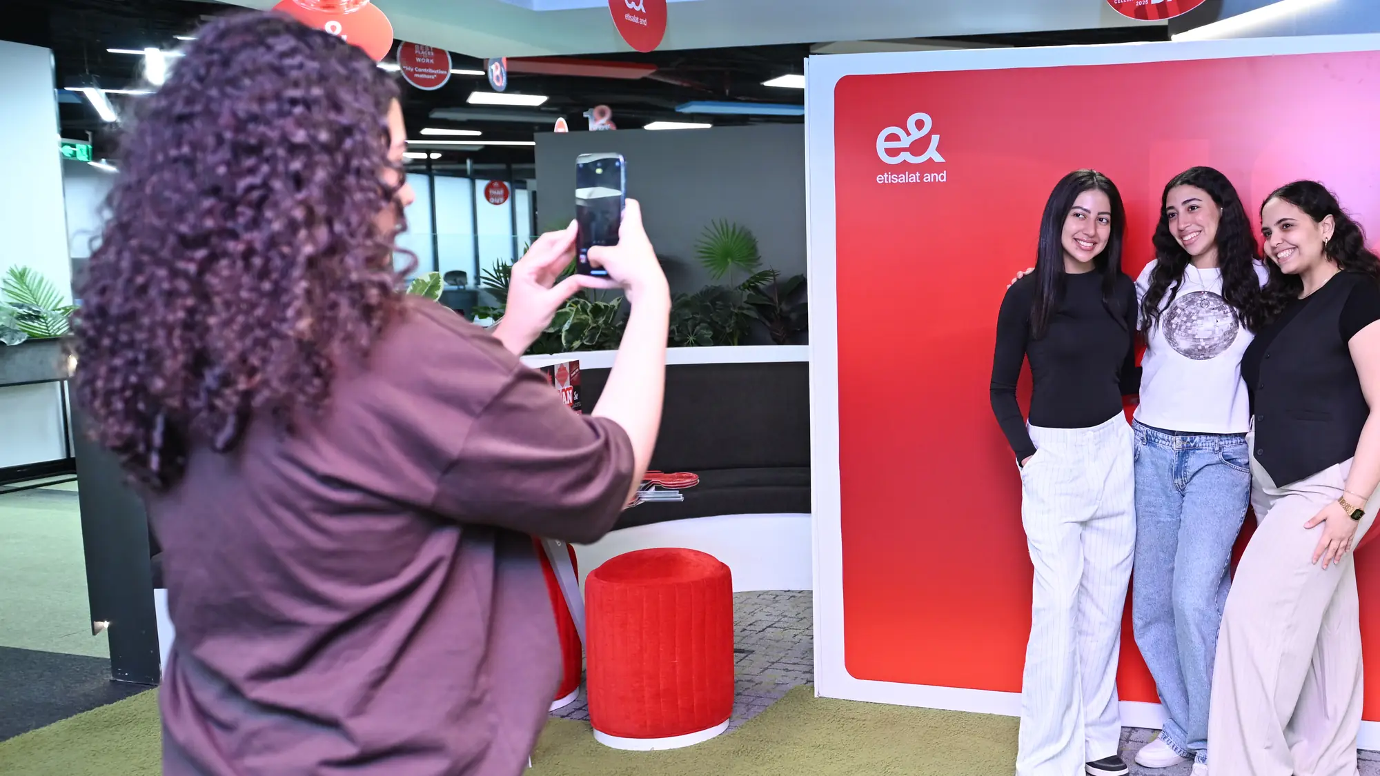 A colleague snaps a phone photo of three smiling friends at an office celebration