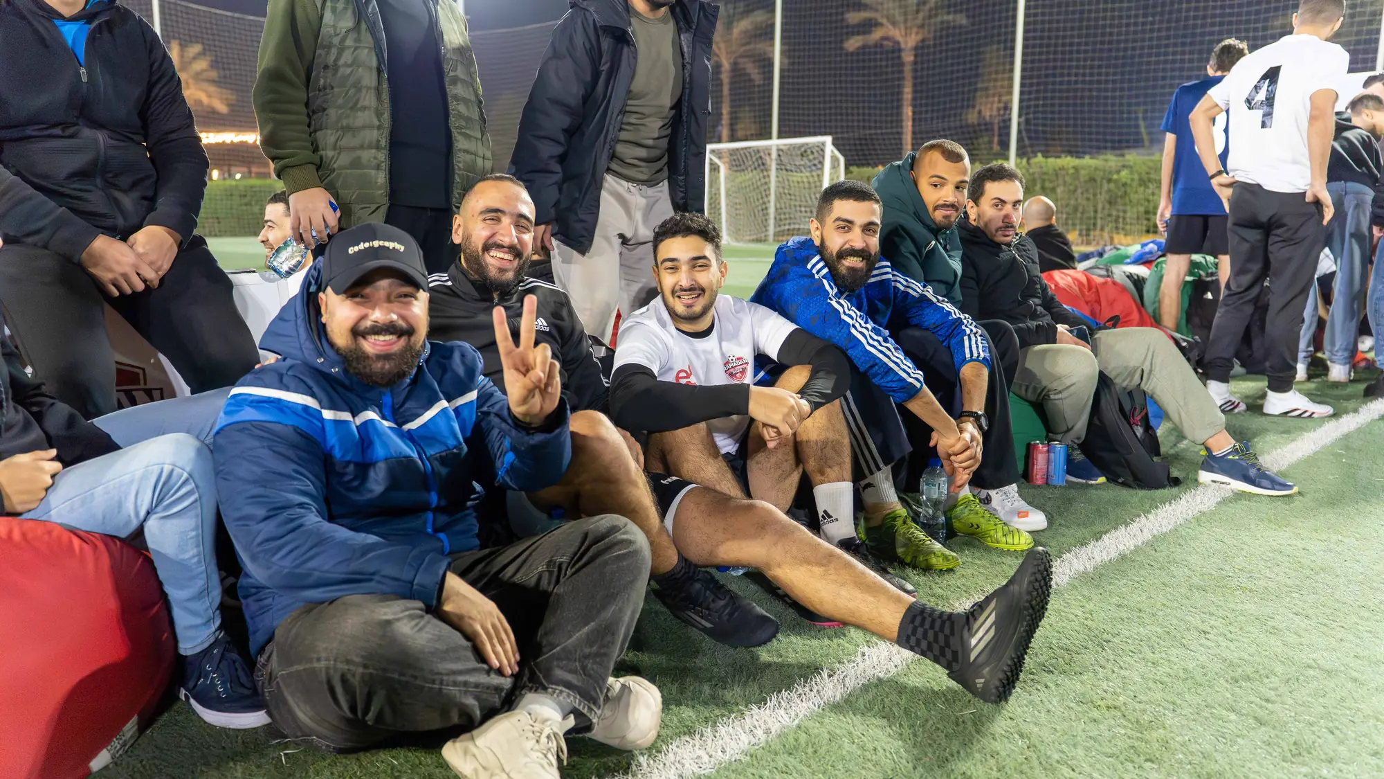 Smiling players and supporters relax on the pitch sideline at night