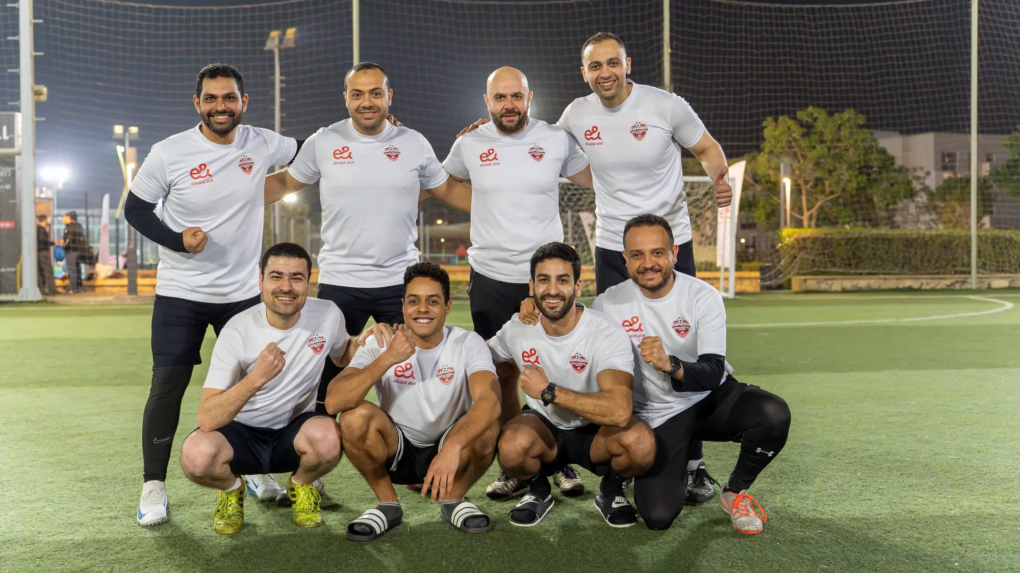 An e& Egypt employee football team in matching shirts poses on a floodlit pitch