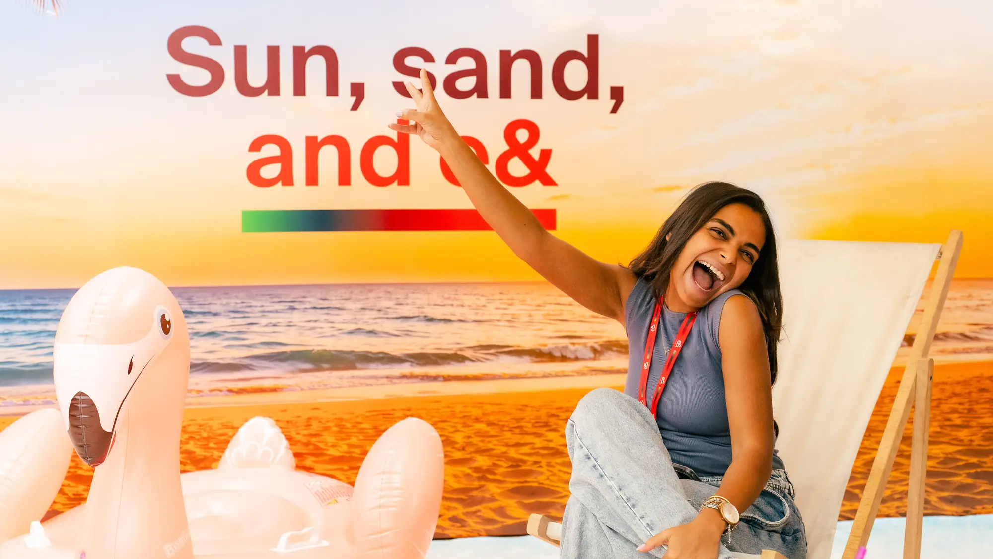 Smiling employee cheers from a deckchair at an indoor beach set with sunset backdrop