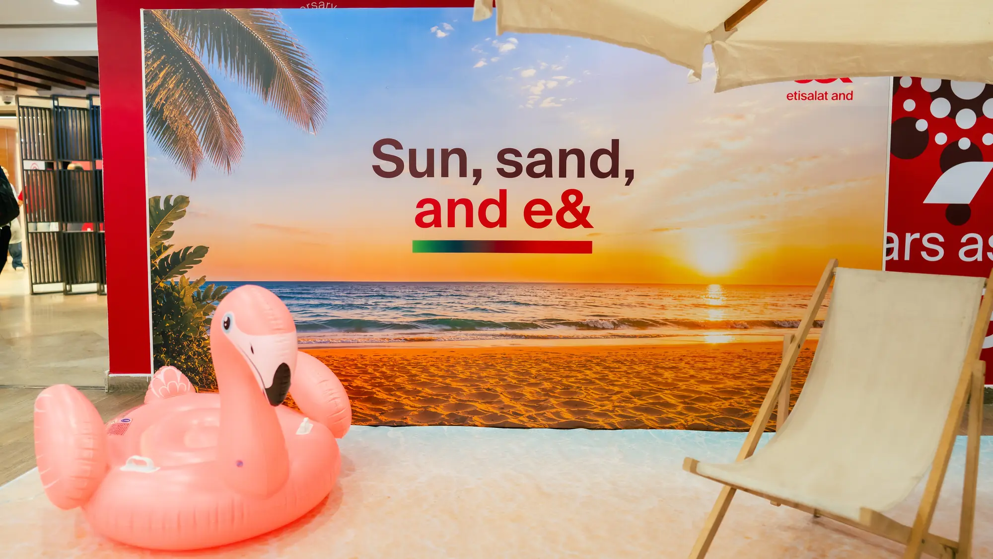 Office beach corner with sand, parasol, deckchair and inflatable flamingo before a sunset backdrop