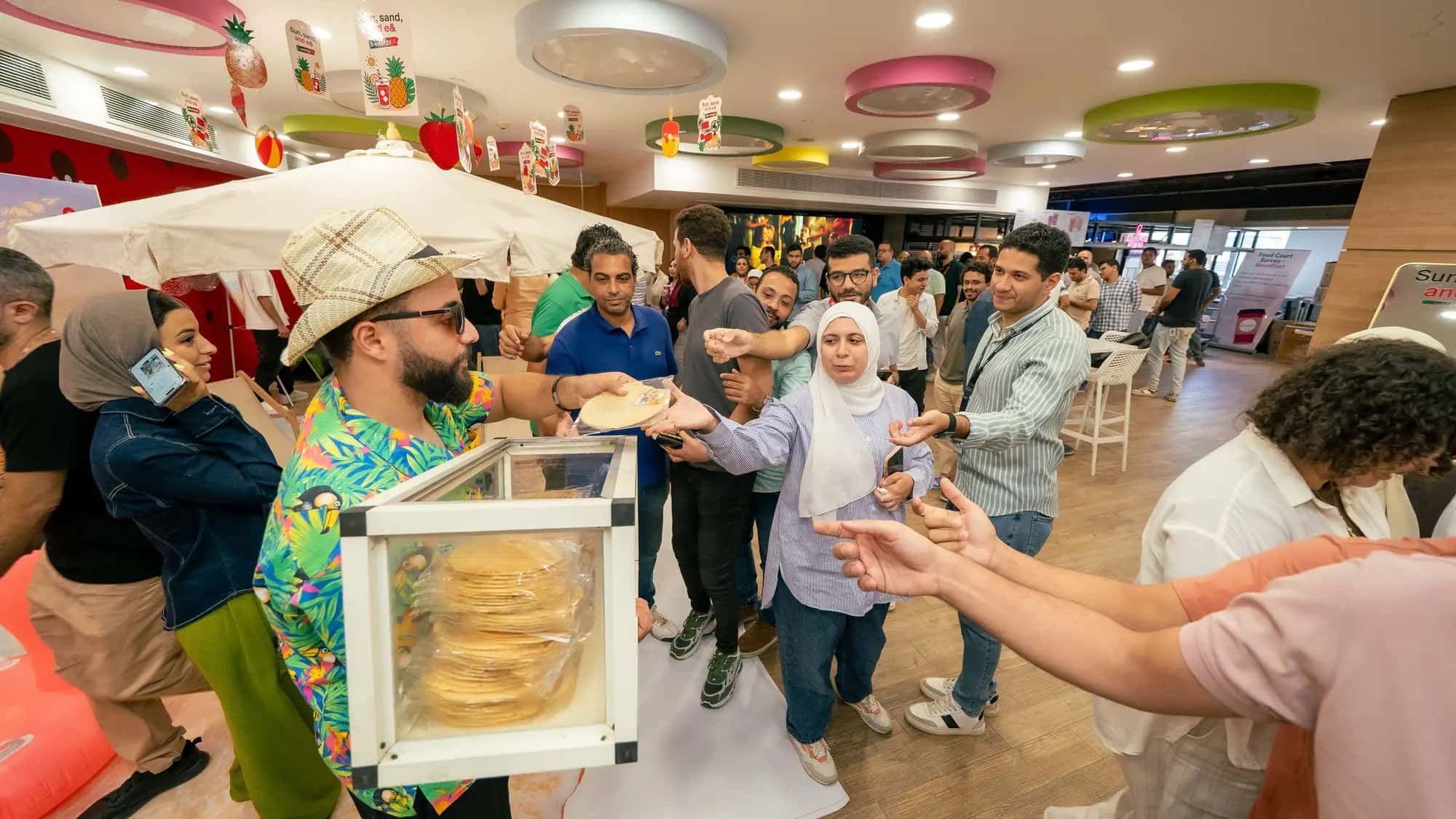 Costumed beach vendor hands out snacks to a lively crowd of colleagues in the office