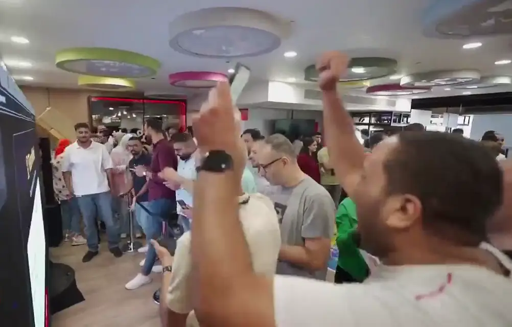 Employees cheering and raising fists during a live team game in a busy office hall