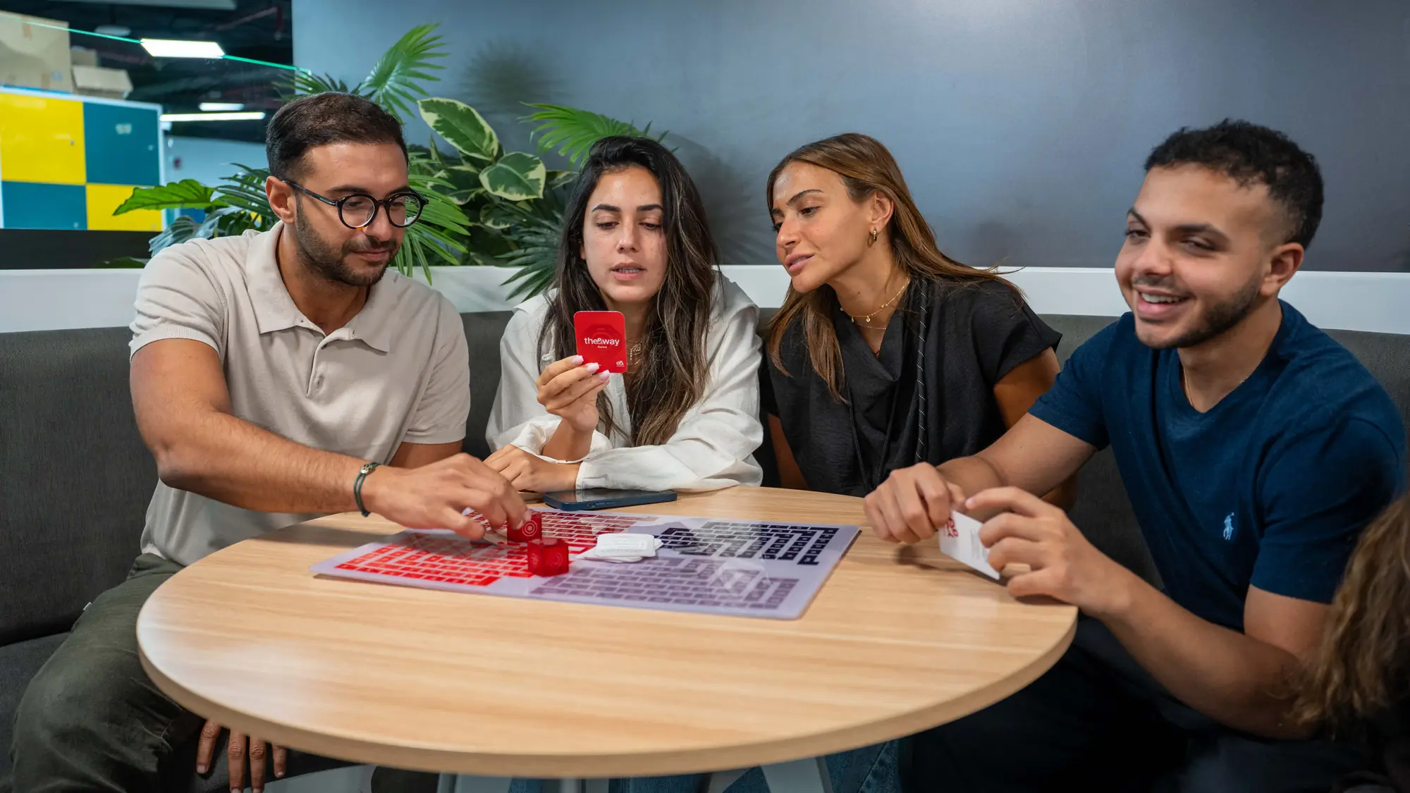 أربعة زملاء يضحكون معاً حول طاولة وهم يلعبون لعبة لوحية عن القيم