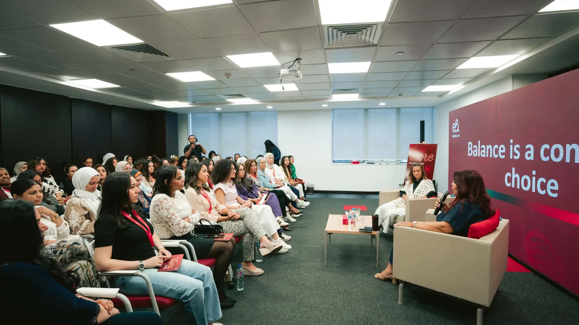 A full room of women colleagues listening to a panel conversation at a workplace event