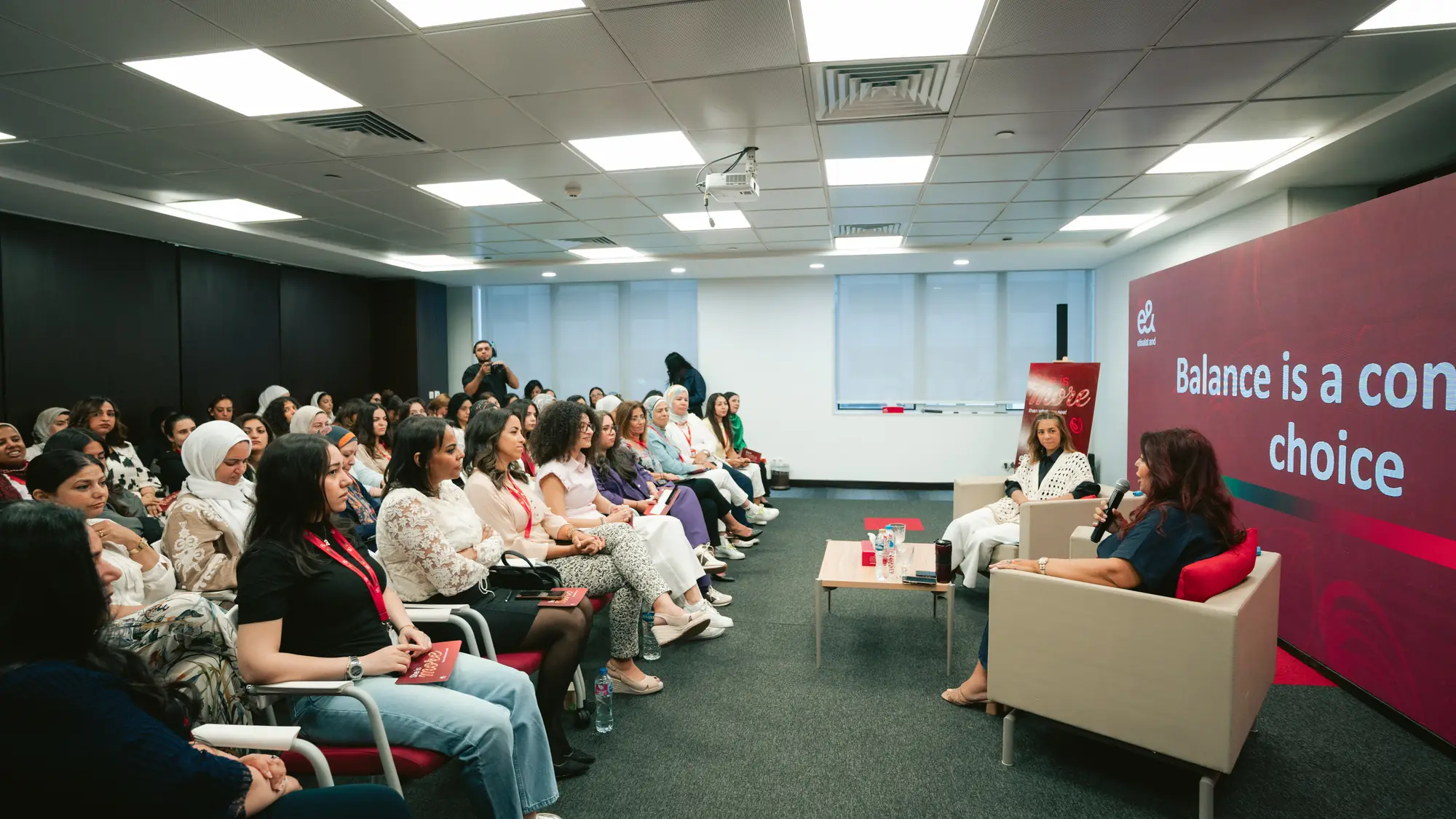 A full room of women colleagues listening to a panel conversation at a workplace event